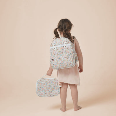 Child wearing an Olli Ella Kids See-Ya Backpack with a pastel floral and butterfly print while carrying a matching travel bag