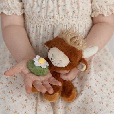 Binky Pets plush Highland cow cuddled by a child in a floral dress alongside a small green flower toy with a yellow centre