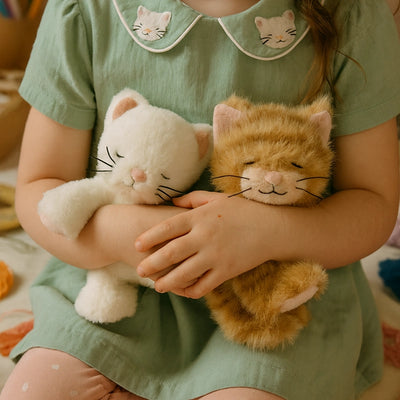 Child cuddling two soft plush kittens in white and ginger with embroidered faces and whiskers while wearing a green cat collar dress from Dinkum Pets