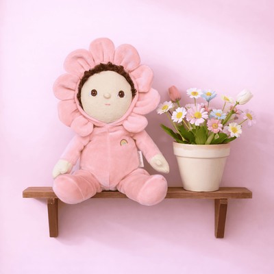 Dinky Dinkums pink flower plush doll seated on a wooden shelf beside a potted bouquet of colourful flowers against a soft pink background