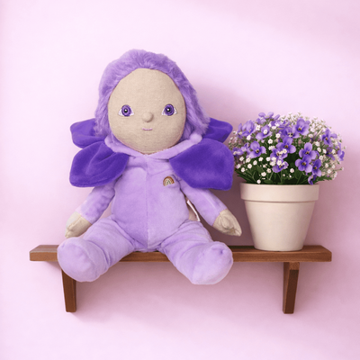 Dinky Dinkums purple plush doll seated on a wooden shelf beside a potted violet flower against a soft pink background for imaginative play