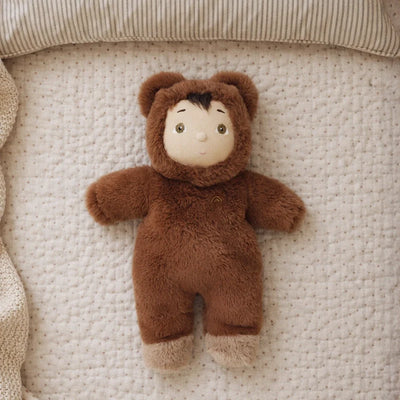 Brown bear Cozy Day Dinkum soft toy lying on a quilted cream blanket with a sweet embroidered face and fuzzy ears and paws