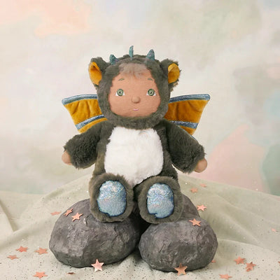 Cozy Dinkums dragon plush doll with soft gray fur white belly blue feet and golden wings sitting on rocks surrounded by pink star shapes