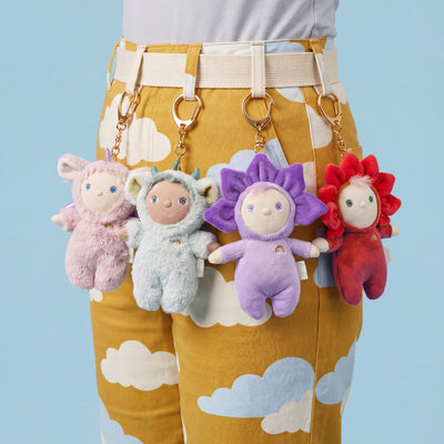 Four soft plush bag charms in pastel pink blue purple and red clipped to mustard cloud print trousers including a red dragon charm from Rainbow Realm