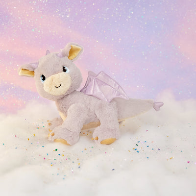 Lavender Dinkum Pets plush dragon toy with soft fur shimmering wings and embroidered eyes posed on a dreamy pastel cloudscape with scattered sparkle confetti