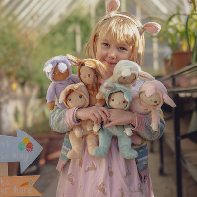 Child hugging six pastel bunny dolls from the Dinky Dinkums Fluffle Family in a garden setting, showcasing soft floppy ears and cuddly imaginative play by Dinky Dinkums