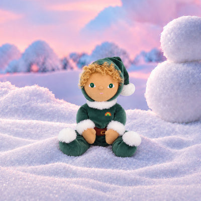 Plush doll with curly golden hair and embroidered green eyes, dressed as a Christmas elf in a dark green velvet suit and pointed hat with white fluffy trim, a brown belt, and a small rainbow patch on the chest.