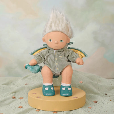 Toy figure with white hair, green outfit, and fairy wings on a beige pedestal against a soft, multicolored background.