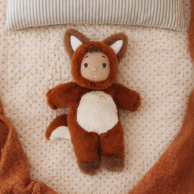 Cozy Dinkums Freddy Fox plush fox doll in a rust brown costume with a white belly and tail tip lying on a soft textured bed