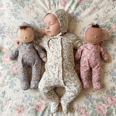 Sleeping baby nestled between two floral print Dozy Dinkums dolls on a vintage floral quilt
