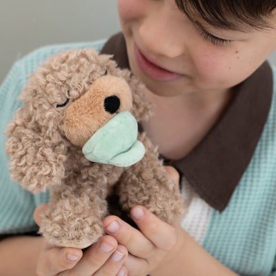 Child cuddling Dinkum Pets Binky Puppy Benny a soft curly plush dog with a weighted body and mint green muzzle for imaginative play