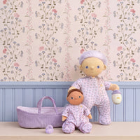 Two dolls in matching outfits with a baby basket against a floral wallpapered wall.