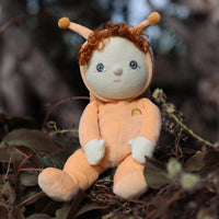 Dinky Dinkum Dolls Scottie Snail soft orange doll with curly hair and antennae sitting among woodland leaves outdoors with a small rainbow detail on its chest