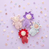 Four colorful plush keychains on a light purple background with flowers.