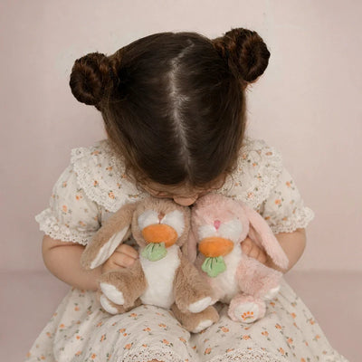 Child holding two plush bunnies against a pink background