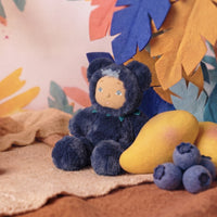 Cozy navy bear plush doll with a soft hooded outfit seated beside blueberries and yellow fruit in a colourful woodland inspired setting by Dinkum Dolls by Olli Ella