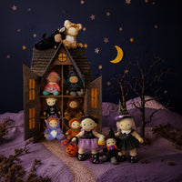 A styled collection of handmade plush dolls arranged around a miniature haunted house diorama at night. The dolls wear various Halloween costumes, including witch, pumpkin, and animal themes, set against a dark blue starry sky backdrop with a crescent moon.