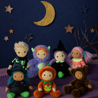 A group of seven plush Halloween dolls dressed in various costumes, arranged on a purple surface against a dark blue background decorated with a gold crescent moon and wooden stars.