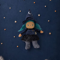 A witch doll with teal hair, wearing a dark blue pointed hat with a silver crescent moon, a dark blue dress, and striped socks, floating against a dark blue starry background with white clouds at the bottom.