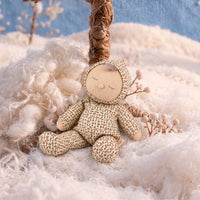 Soft baby doll with sleepy embroidered closed eyes, a smiling mouth and a tuft of brown hair, wearing a cream footed sleepsuit and matching bonnet printed with small red and green sprigs.