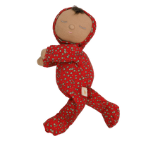 Soft baby doll with sleepy embroidered closed eyes, a smiling mouth and a tuft of dark brown hair, wearing a red footed sleepsuit and matching bonnet with a ditsy floral print, button placket, and a small embroidered rainbow.