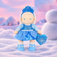 Plush doll with white hair, blue eyes and rosy cheeks, wearing a blue velvet tiara, a sequinned blue dress with sheer sparkly sleeves and a tulle skirt, white frilled socks, light blue shoes, and a blue heart-shaped bag with an embroidered snowflake.