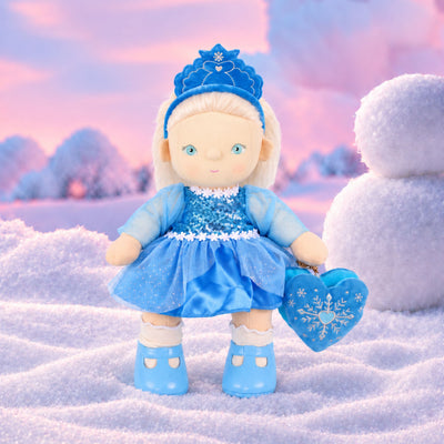 Plush doll with white hair, blue eyes and rosy cheeks, wearing a blue velvet tiara, a sequinned blue dress with sheer sparkly sleeves and a tulle skirt, white frilled socks, light blue shoes, and a blue heart-shaped bag with an embroidered snowflake.