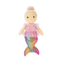 A mermaid-themed plush doll with a pale yellow face and hands, blonde hair in a bun, wearing a pink top with a small rainbow detail and a shimmering iridescent mermaid tail, isolated on a white background.