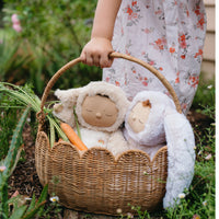 Natural rattan petal basket with two soft dolls and a carrot held by a child in a garden setting、】【