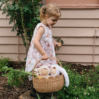 Child carrying a natural rattan Petal Basket filled with plush lamb toys and a soft blanket outdoors. Olli Ella basket for imaginative play and Easter hunts