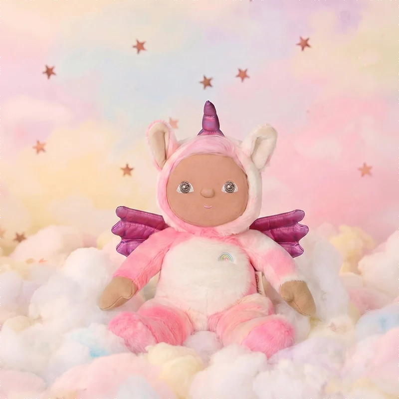 Pink unicorn plush doll with purple wings and a tiny rainbow on its belly sitting among pastel clouds against a dreamy starry backdrop from Dinky Dinkums