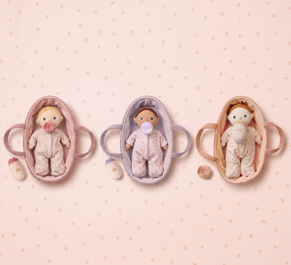 Three baby dolls in miniature cribs on a pink polka dot background