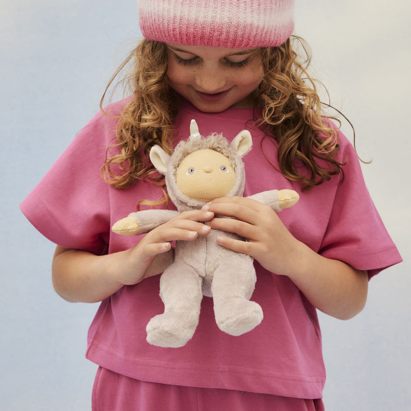 Child in a pink outfit cuddling a soft lilac unicorn doll with a horn and floppy ears from Dinky Dinkums