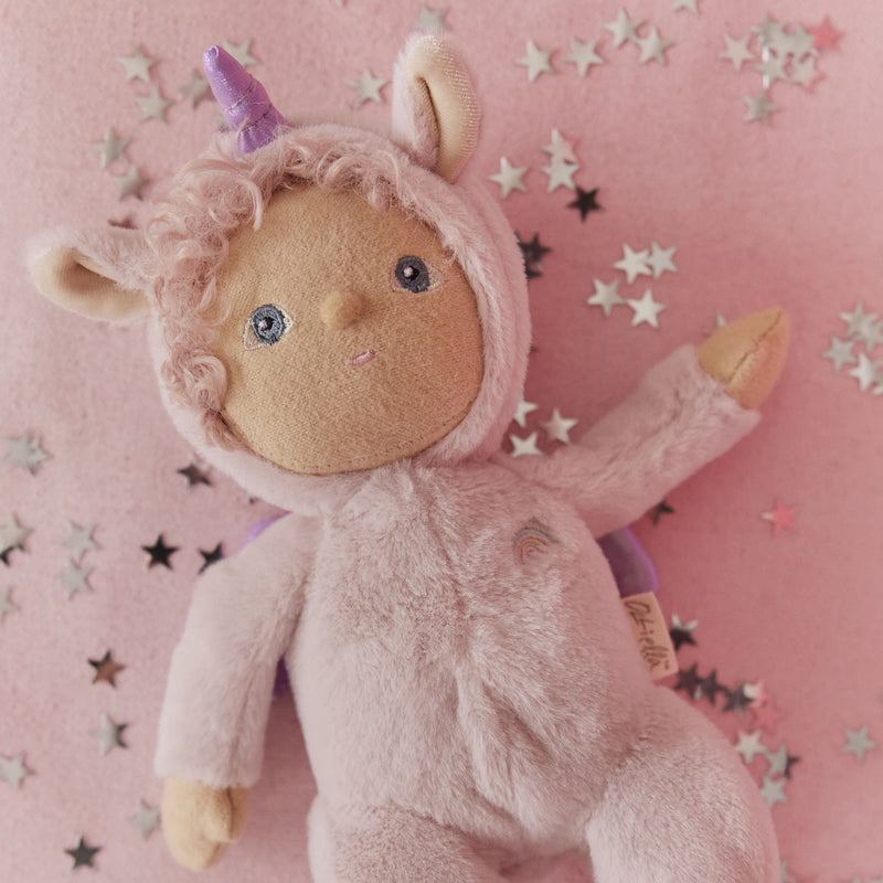 Dinky Dinkums Una Unicorn soft pink plush doll with a purple horn and embroidered face lying on a pink starry background