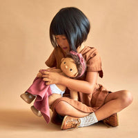 Plush baby doll with brown hair being dressed up by a kid in brown dress and shoes