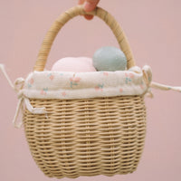 Handwoven rattan berry basket with a cream floral cotton liner and pastel eggs inside held by the handle against a soft pink background from Olli Ella Kids Rattan