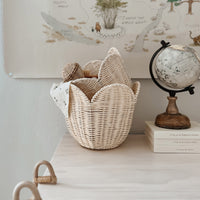 Olli Ella Nursery buttercream rattan Lily basket set with a scalloped open weave sits on a nursery shelf beside a vintage globe and storybooks