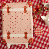 Olli Ella Kids pink kids suitcase with strawberry print and tan leather trim on a red gingham picnic cloth beside fresh strawberries and a tea set