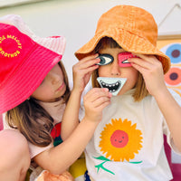 Two children play with Loopy Lucy Funspressions sensory stones by Olli Ella Kids while wearing colorful hats and creating silly facial expressions