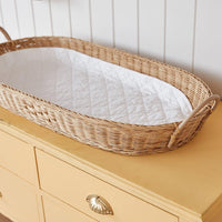 Olli Ella Nursery Bayu rattan changing basket with white cushioned liner and tan handles on a wooden nursery dresser
