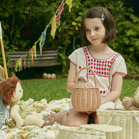 Child holding a natural rattan basket while playing outdoors with a doll during a garden picnic styled by Olli Ella Home
