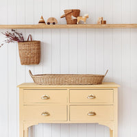Olli Ella Nursery Bayu rattan changing basket displayed on a vintage yellow dresser in a calm nursery with woven storage and wooden toys