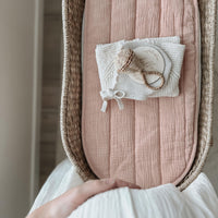 Olli Ella Nursery rose organic cotton liner fitted inside a woven changing basket with a soft white cloth and small baby accessory resting on top