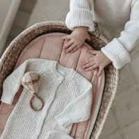 Rose organic cotton liner inside a woven changing basket with a knitted baby outfit and wooden rattle Olli Ella Nursery nursery essential for gentle everyday use