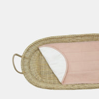 Woven changing basket fitted with a soft lightly padded rose cotton liner from Olli Ella Nursery showing its curved edge and white underside