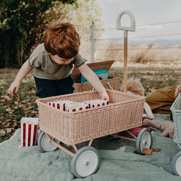 Child loading treasures into the rose rattan Wonder Wagon by Olli Ella during imaginative outdoor play