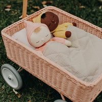 Pink rattan Wonder Wagon holding two soft dolls under a quilt outdoors on grass in a charming Olli Ella Kids design for imaginative play