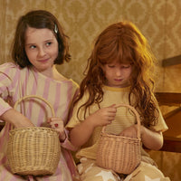 Two children hold woven rattan baskets during imaginative play with the Olli Ella Home Rose Berry Basket in soft rose pink