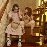 Two children playing on a staircase with small rose and natural rattan baskets from Olli Ella Home