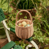 Rose rattan basket with a woven handle holding Easter eggs and a small chick in a leafy garden setting from Olli Ella Home